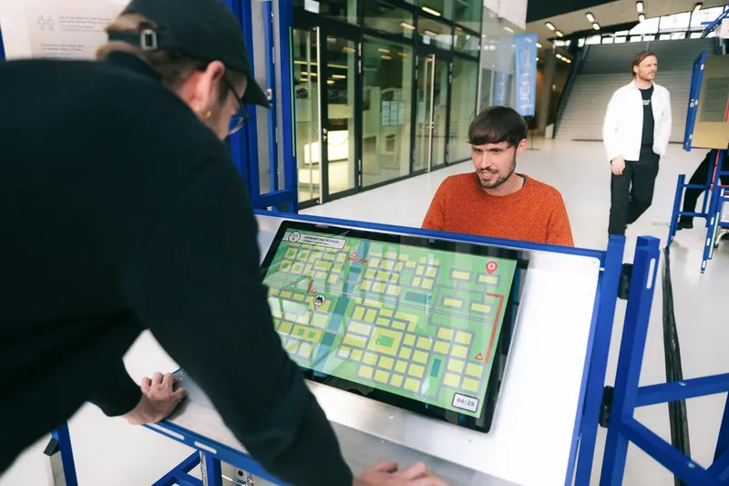 Two visitors play a game together on opposite sides of a station. One is examining a city map.