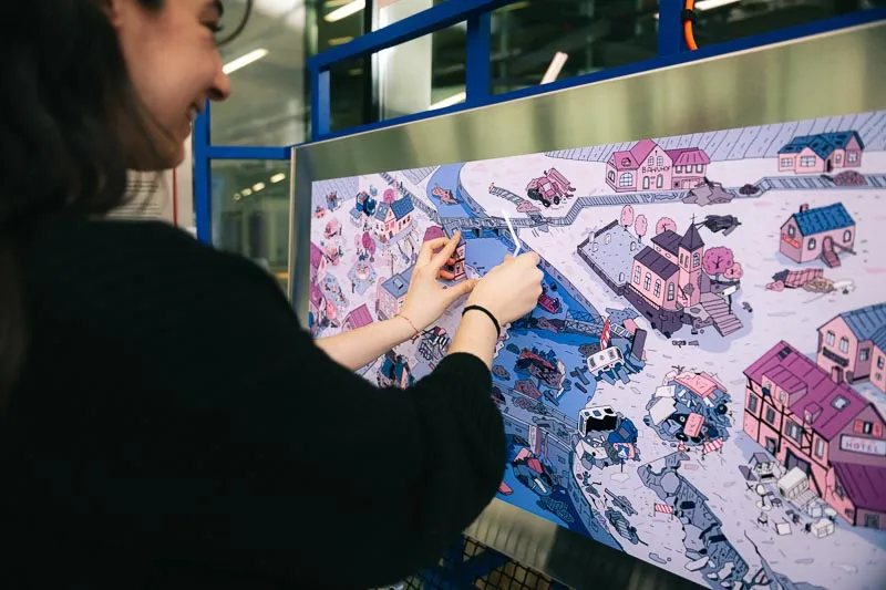 A woman places a puzzle piece on an illustrated panel depicting a flooded town.