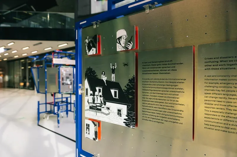 Close-up of an exhibition panel with comic-style illustrations and German and English text on a metal board.